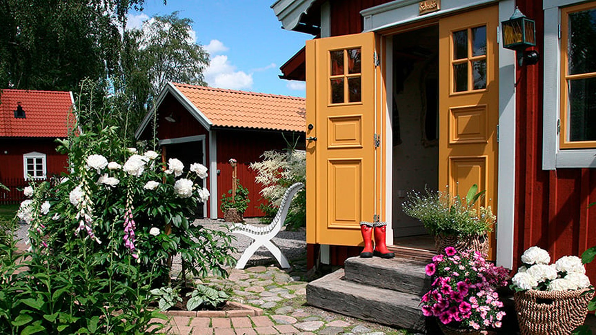 En rödmålad stuga med planterade blommor utanför.